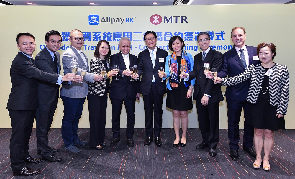 (左起) Alipay Payment Services(HK) Limited業務總裁連炳坤、Alipay Payment Services(HK) Limited財務總裁黃漢森、Alipay Payment Services(HK) Limited營運總裁兼Alipay Financial Services HK暫任行政總裁文明軒、Alipay Payment Services(HK) Limited行政總裁陳婉真、長江和記實業集團聯席董事總經理及Alipay Payment Services(HK) Limited董事局主席霍建寜、港鐵公司主席馬時亨、港鐵公司商務總監楊美珍、港鐵公司車務總監劉天成、港鐵公司技術工程總監顏永文及港鐵公司公司事務總監蘇家碧一同祝酒，慶祝雙方簽訂應用二維碼付費的合約。